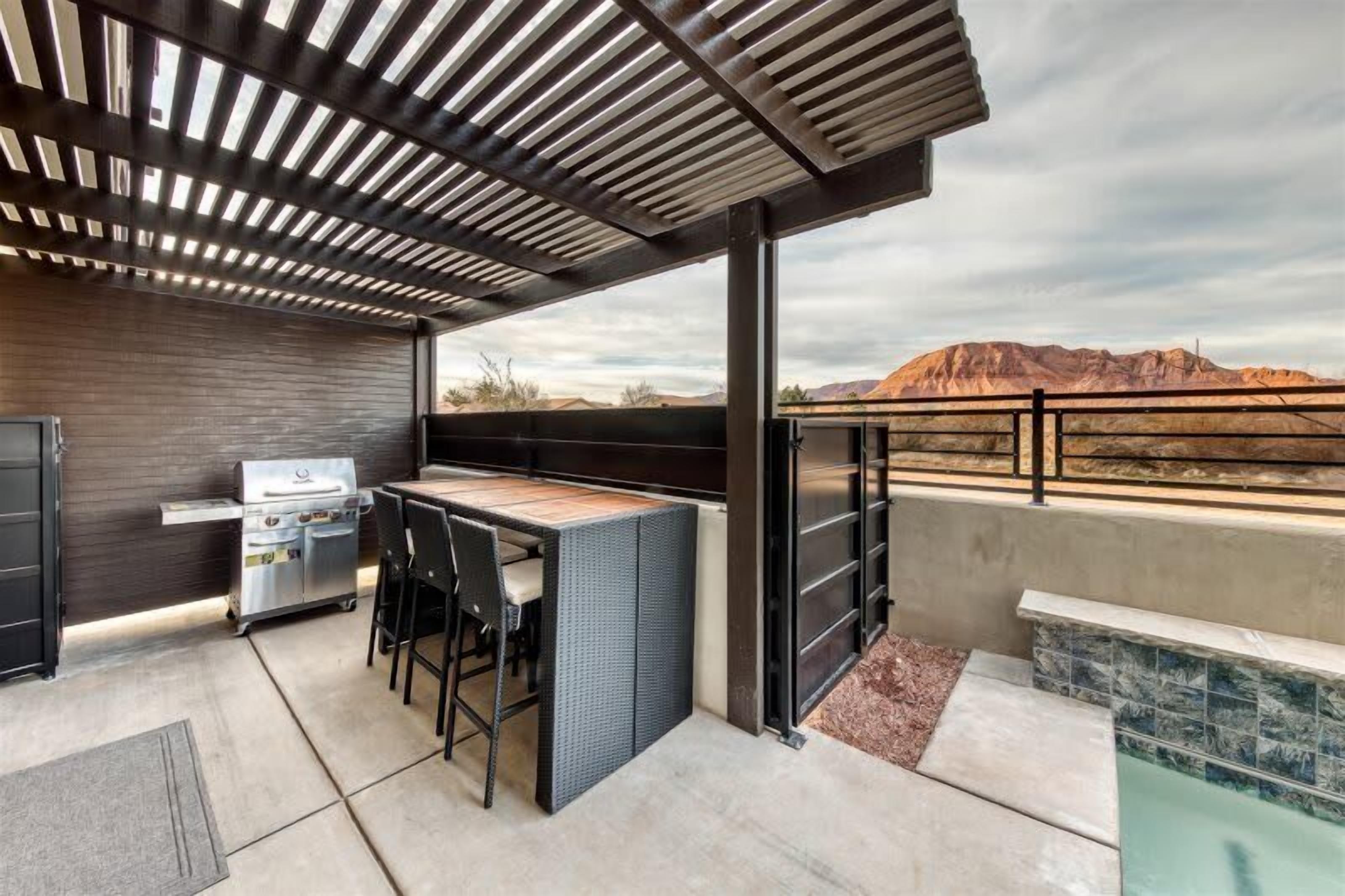 An outdoor patio with a grill, seating, and a view of a mountainous landscape.