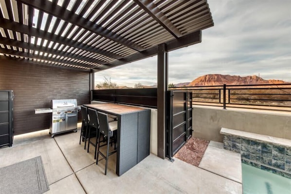 An outdoor patio with a grill, seating, and a view of a mountainous landscape.