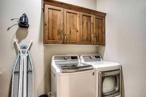 A laundry area with a washing machine and dryer, wooden cabinets above, and a drying rack.