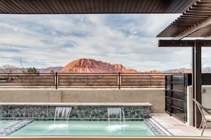 A pool with a waterfall feature, surrounded by a metal railing, with a mountain in the background.