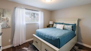 Een slaapkamer met een bed, een raam met gordijnen, een bedlampje en een wanddecoratie.