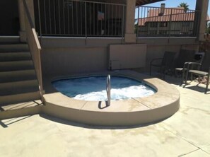 A circular hot tub with a metal ladder, surrounded by a concrete deck.