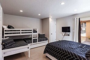 A bedroom with bunk beds, a single bed, a television, and a door leading to an outdoor area.