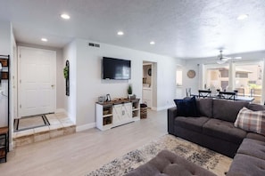 A modern living room with a sofa, a television, a cabinet, and a door. - The MVP at Sports Village | Pet Friendly Retreat (Saint George)