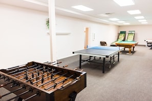 A room with a foosball table, a ping pong table, and two pool tables.