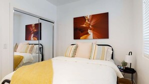 A hotel room with a bed, a nightstand, a clock, and two wall-mounted paintings.