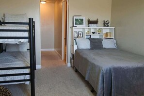 Une chambre avec des lits superposés, une table de chevet avec une lampe et une étagère murale ornée d’objets décoratifs.