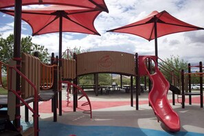 Une aire de jeux avec un toboggan rouge, des structures d’escalade et des tables de pique-nique.