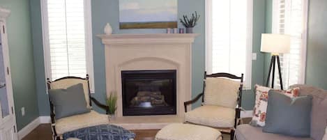 Una habitación con chimenea, dos sillones, un sofá y una lámpara.