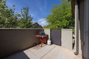 Une terrasse équipée d’un barbecue et d’une bouteille de propane, le tout délimité par un petit muret et un portail.
