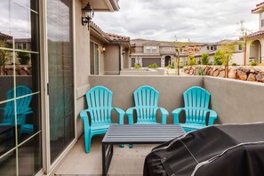 Une terrasse avec trois chaises turquoise et une table, une porte vitrée et une vue sur les maisons voisines.