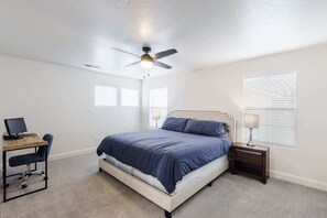 Une chambre à coucher comprenant un lit, un bureau, une chaise, une table de chevet et un ventilateur de plafond.