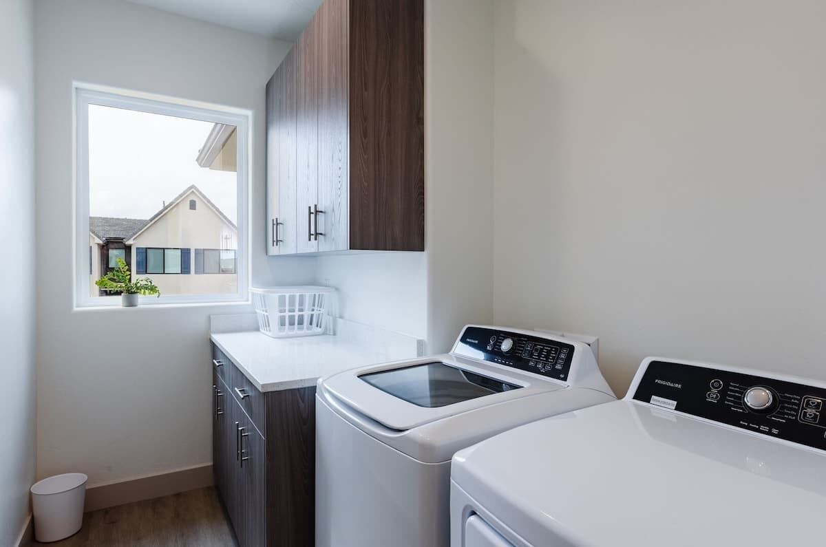 A laundry room with a washing machine, dryer, and a window with a view of a house.