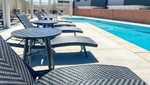Un espace aménagé au bord de la piscine, avec des chaises longues et des tables, une piscine, et des maisons modernes en arrière-plan.