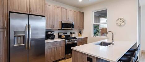 A modern kitchen with wooden cabinets, stainless steel appliances, a central island with bar stools, and a clock on the wall.