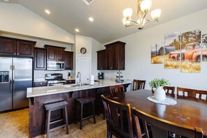 A modern kitchen with dark wood cabinets, stainless steel appliances, a central island with bar stools, and a dining table with chairs.