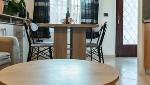 A dining area with a round wooden table, two chairs, a potted plant, and a window with curtains. - Holiday apartment with terrace (Medulin)