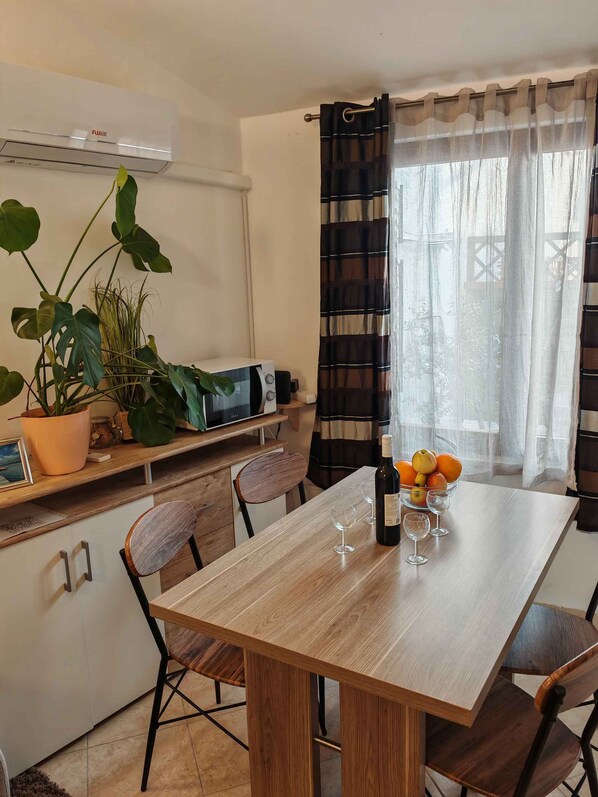 A dining area with a wooden table, chairs, a potted plant, a microwave, and a window with curtains. - Holiday apartment with terrace (Medulin)