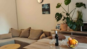 A modern living room with a sofa, a dining table with chairs, a clock, a potted plant, and a bowl of fruit. - Holiday apartment with terrace (Medulin)