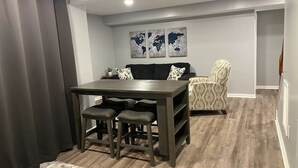 Een gezellige, compacte leefruimte met een eettafel en vier krukken, een bank en een fauteuil met een patroon.