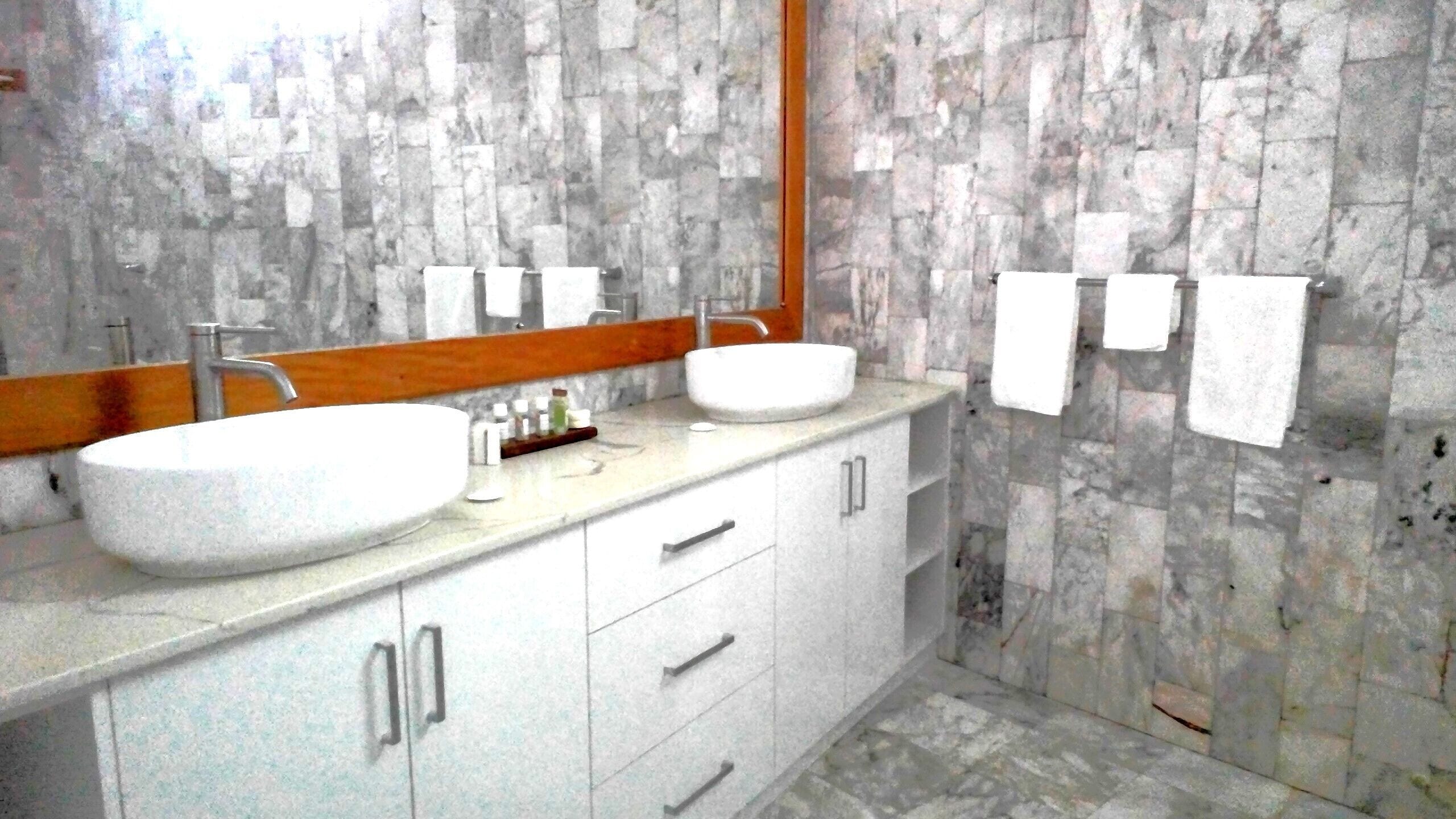 A bathroom with two large white sinks, a wooden vanity, and a marble backsplash.