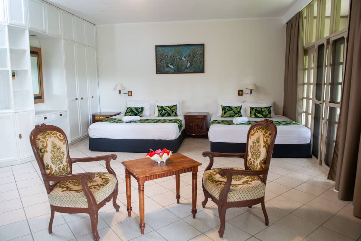 Habitación de hotel con dos camas, una mesa de madera, dos sillas, un cuadro en la pared y un ventanal con cortinas.