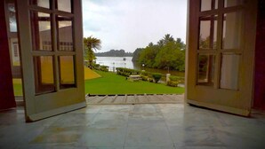 An open door leading to a balcony with a view of a river, a grassy area, and a row of trees. - Yatu Lau Lagoon Resort  (Pacific Harbour)