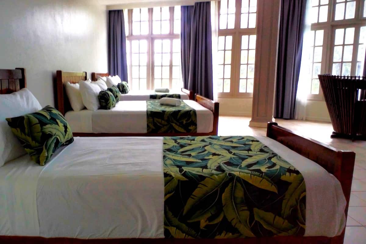 Habitación de hotel con dos camas, un ventanal con cortinas y un cubo de basura.