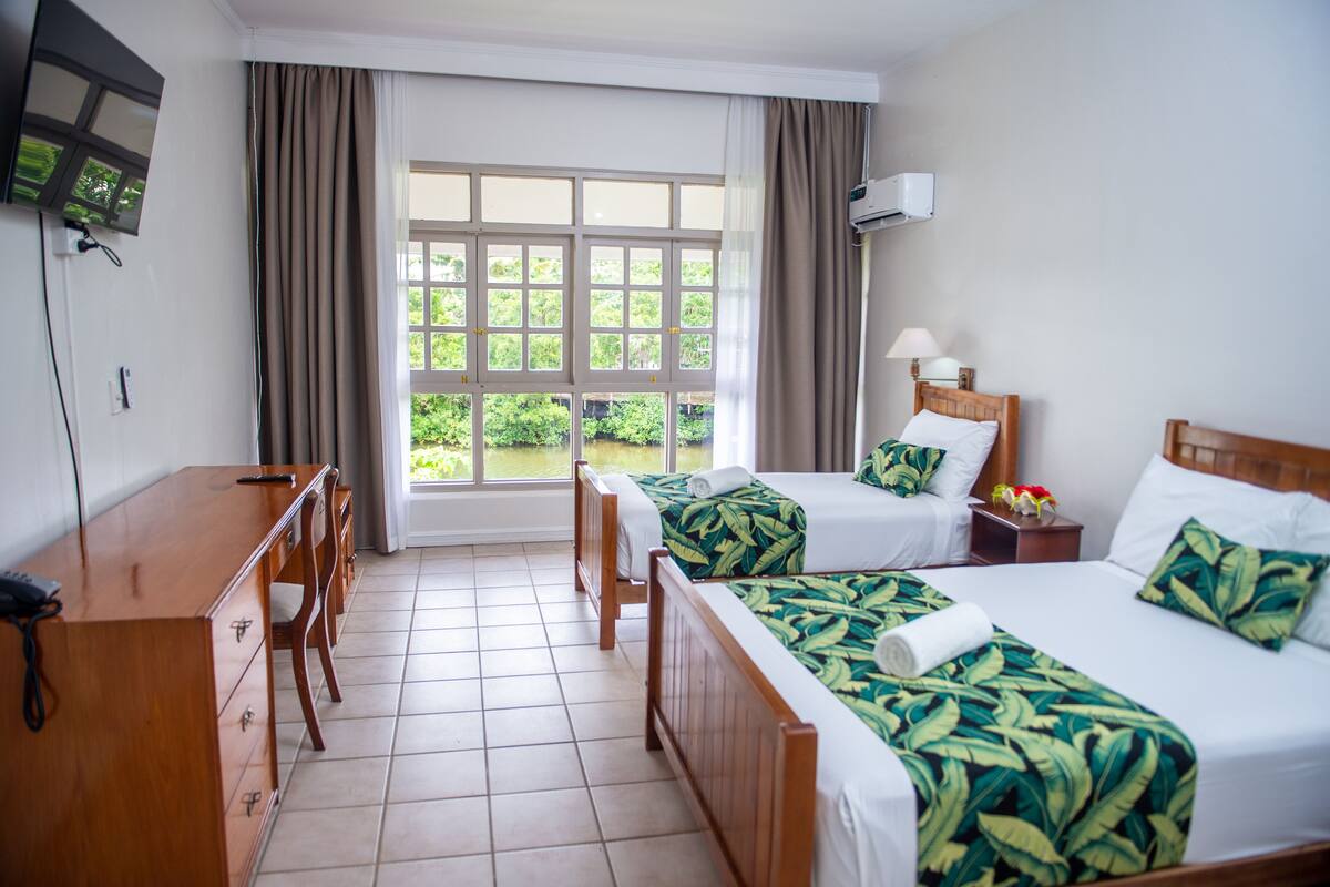 Habitación de hotel con dos camas, un escritorio, una silla, un televisor y una ventana con cortinas.