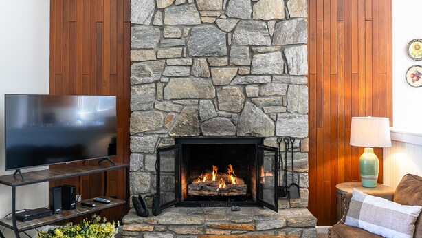 A stone fireplace with a TV on a wooden stand to the left. - Chetola Chestnut 8 - close to downtown Blowing Rock! (Blowing Rock)