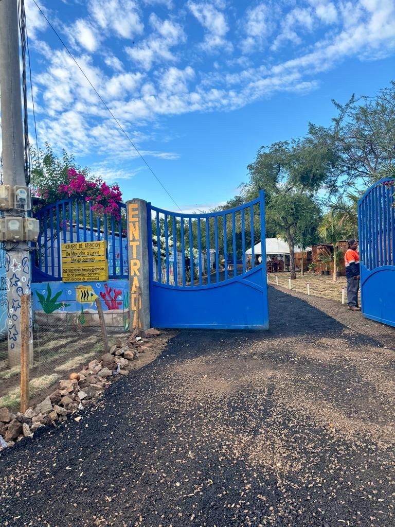A gated entrance with a blue gate, a sign with text, and a person standing nearby.