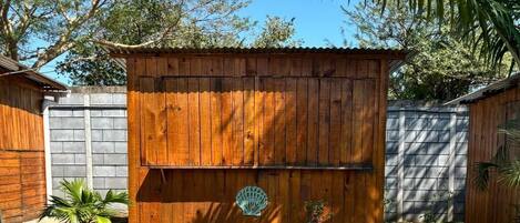 A wooden shed with a circular emblem on the front, surrounded by potted plants and a clear blue sky.