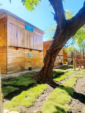 A wooden building with a corrugated metal roof, surrounded by a garden with grass and a tree. - Aqua Beach Resort (San Rafael del Sur)