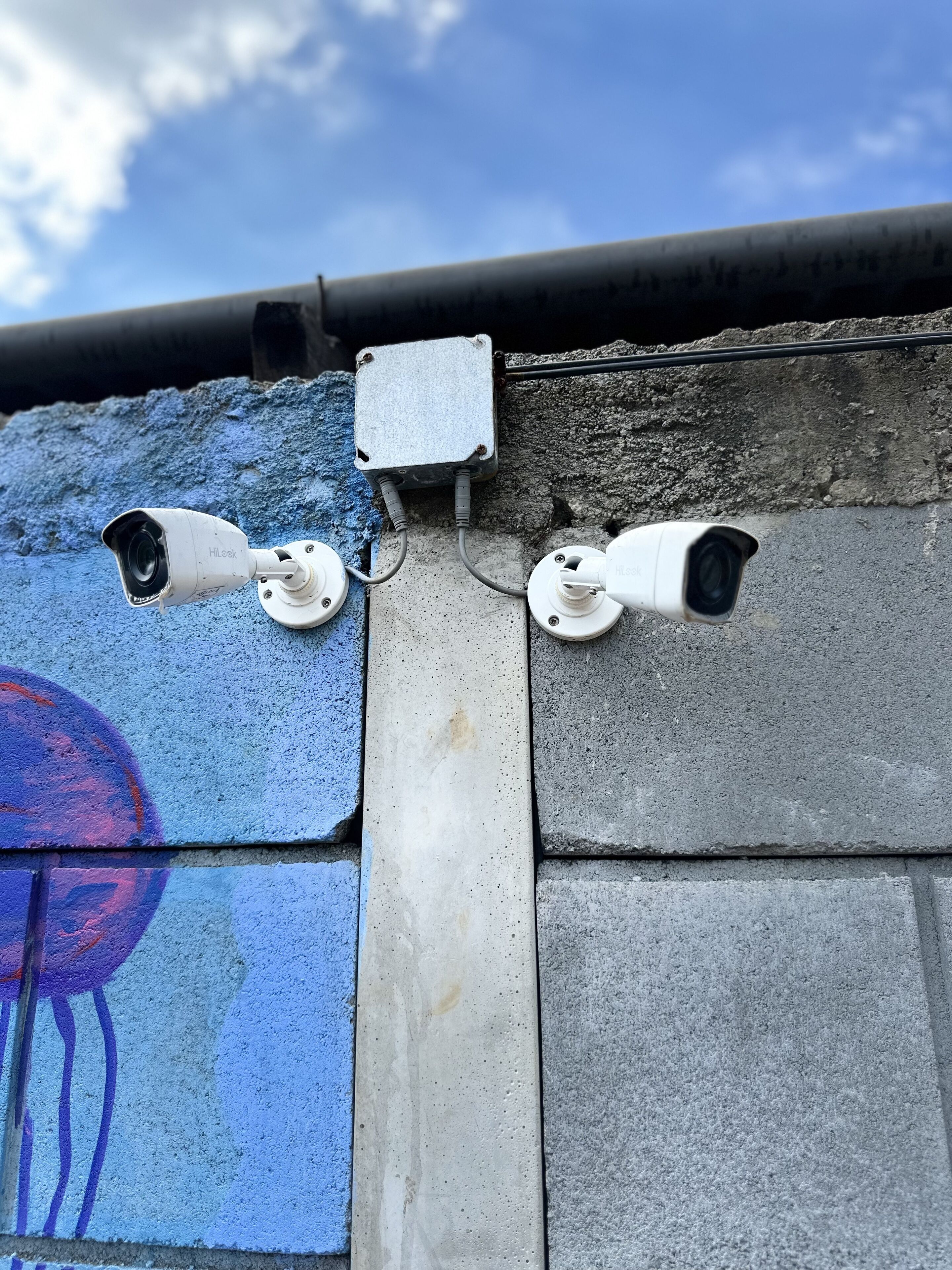 A security camera mounted on a concrete wall with a graffiti mural.