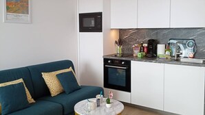 Um espaço compacto com cozinha compacta, um sofá, uma mesa redonda pequena e uma máquina de café.