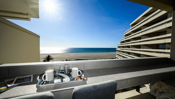 Varanda com bandeja de objetos, vista para a praia e um edifício com várias varandas.