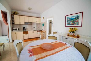 Une cuisine de taille réduite, équipée d’appareils électroménagers de base, un coin repas avec une table et des chaises, et un tableau accroché au mur.
