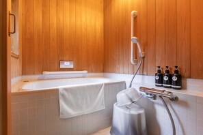 A modern bathroom with a wooden panel wall, a white bathtub, a towel, and three bottles of shampoo.