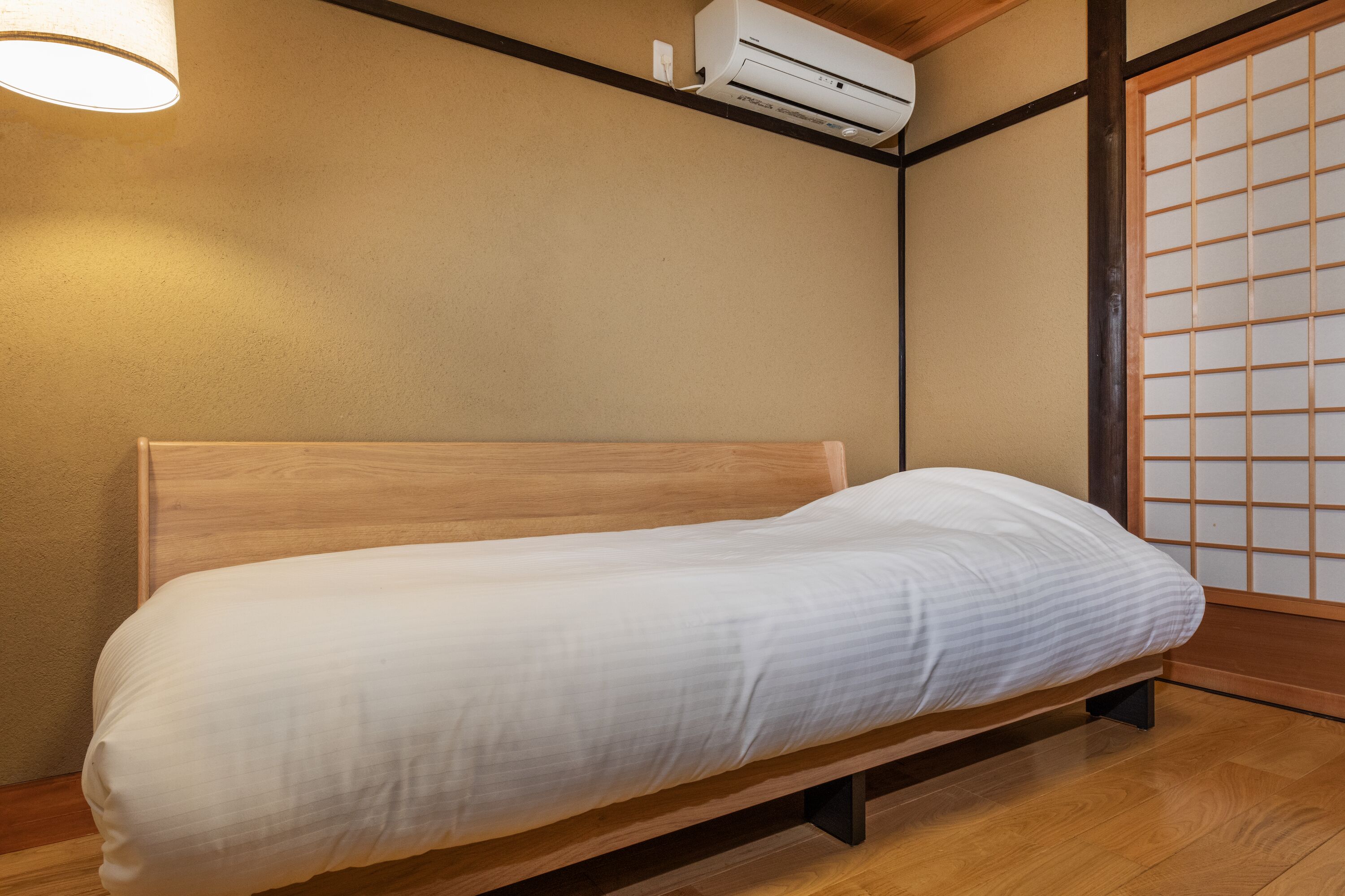A single bed with a wooden headboard in a room with a traditional Japanese shoji screen and an air conditioning unit mounted on the wall.