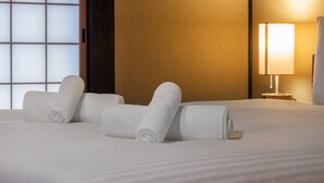 A neatly made bed with rolled white towels, a bedside lamp, and a view of a wooden door. - Shiki Homes Machiya Mei (Kyoto)