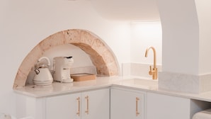 A kitchen with white cabinets, a marble arch, a coffee maker, and a gold faucet. - Dimore Bianche Santa Lucia 17 (Putignano)