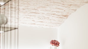 A hotel room with a bed, white linens, a small vase with flowers, and a white wall. - Dimore Bianche Santa Lucia 17 (Putignano)