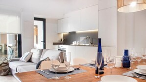 Una cocina moderna con armarios blancos, una mesa de comedor con copas y platos de vino, y un sofá en la sala de estar.