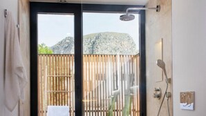 Un baño moderno con una amplia puerta corredera de vidrio que da a un balcón, una bañera blanca, un tocador de madera y una planta en maceta.