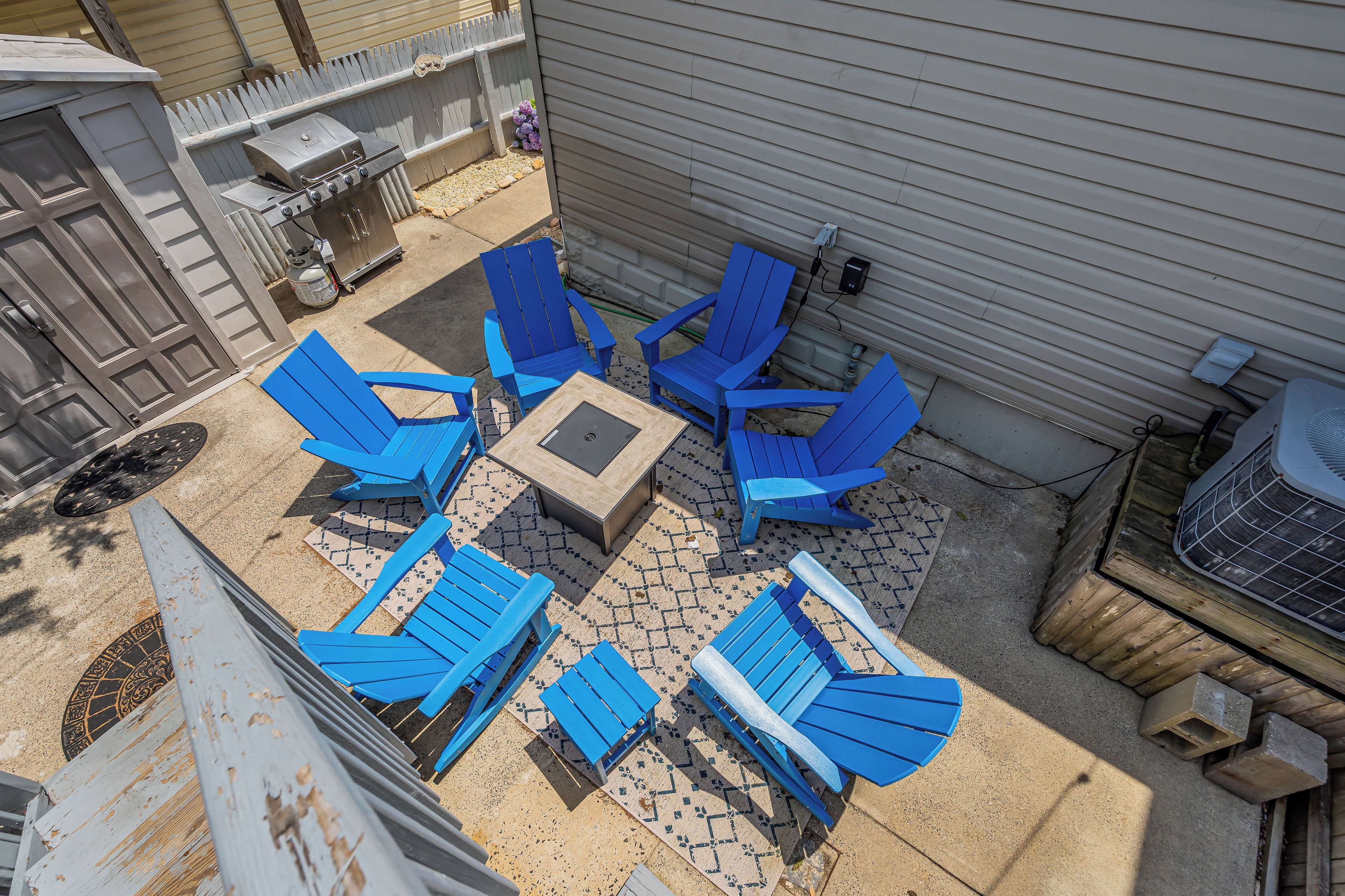 Un patio con sillas Adirondack azules y una pequeña mesa, rodeado de un suelo de hormigón y una valla de madera.