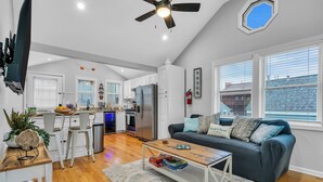 A modern kitchen with white cabinets, a stainless steel refrigerator, and a dining area with a wooden table and chairs. - Professionally Managed | 3 Blocks to Beach (Seaside Heights)