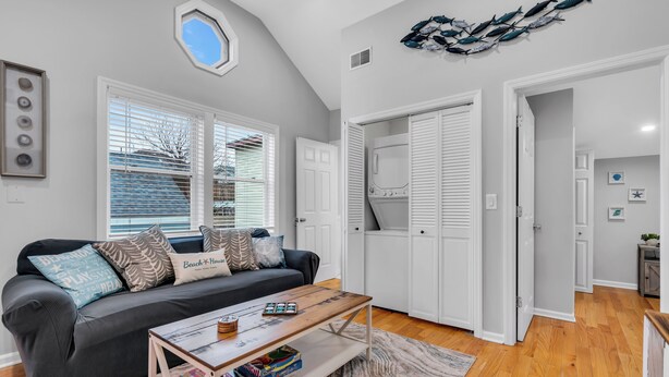 A modern living room with a grey sofa, a coffee table with board games, and a view of the outside through large windows. - Professionally Managed | 3 Blocks to Beach (Seaside Heights)