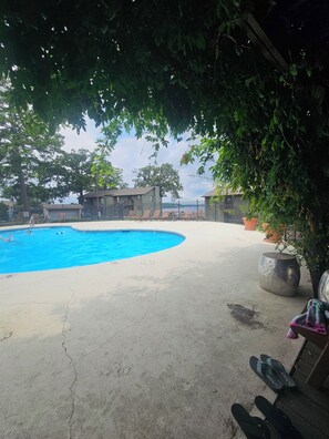 Ein Schwimmbecken mit Liegestühlen, einer Betonplattform und Blick auf ein Gebäude im Hintergrund.