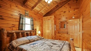 Un dormitorio tipo cabaña de madera con una cama, una ventana con cortinas, una puerta y un ventilador de techo.