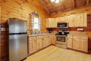A wooden cabin-style kitchen with a stainless steel refrigerator, a microwave, an oven, and wooden cabinets.